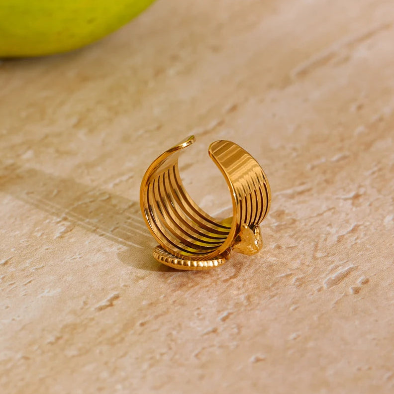 Gold hoop earring on a beige surface with a green apple in the background