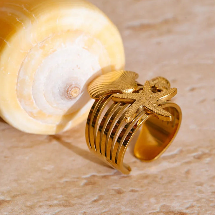 Gold ring with intricate design on a beige shell against a beige background
