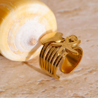 Gold ring with intricate design on a beige shell against a beige background