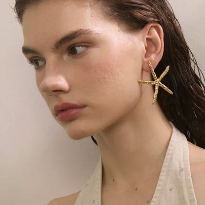 A stack of fashion magazine covers fanned out on a white background, with the top cover featuring a close-up portrait of a woman wearing a gold star-shaped earring.