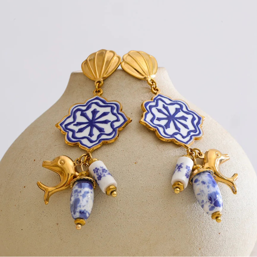 Pair of earrings with blue and white floral designs on a beige stand.