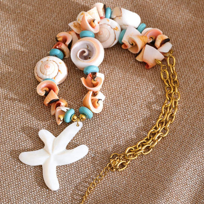 Bracelet with shell beads and a gold chain on a textured surface