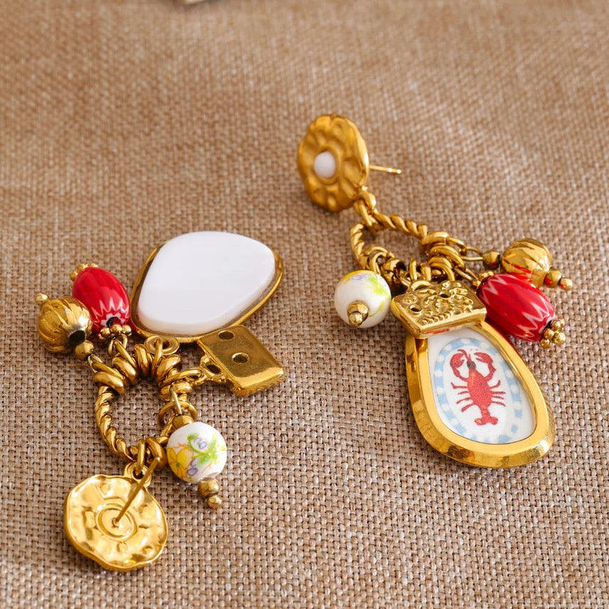 Decorative earrings with gold accents and colorful charms on a textured brown background