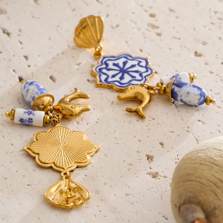 Gold and blue ceramic earrings on a textured beige surface
