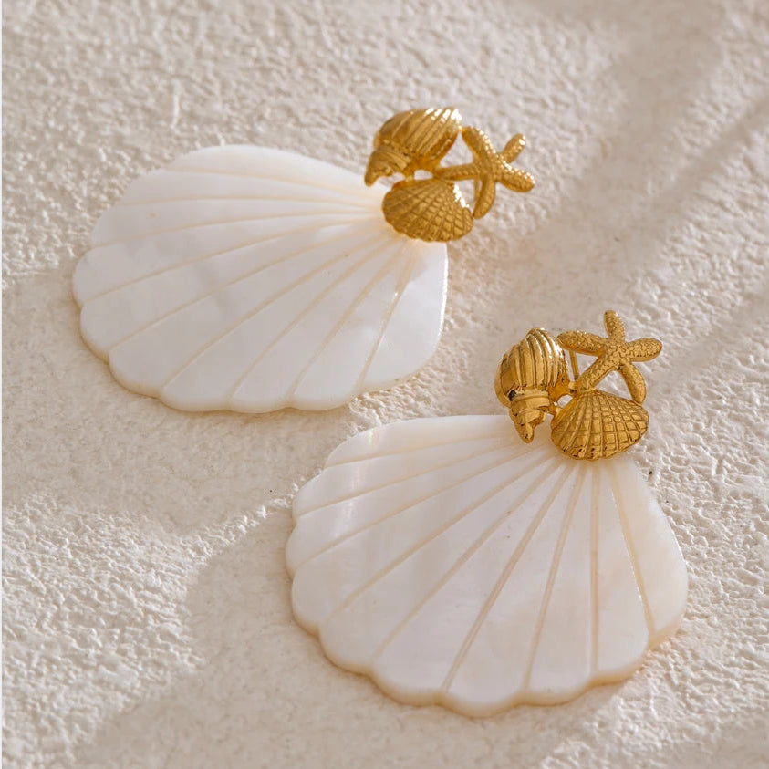Shell-shaped earrings with gold accents on a textured beige background