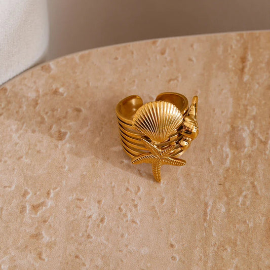 Gold shell-shaped ring on a textured beige surface