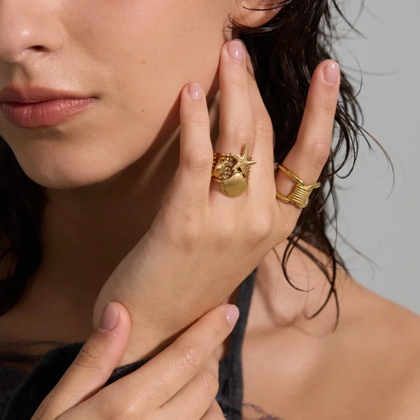 Woman wearing gold rings on fingers and earrings, with a neutral background