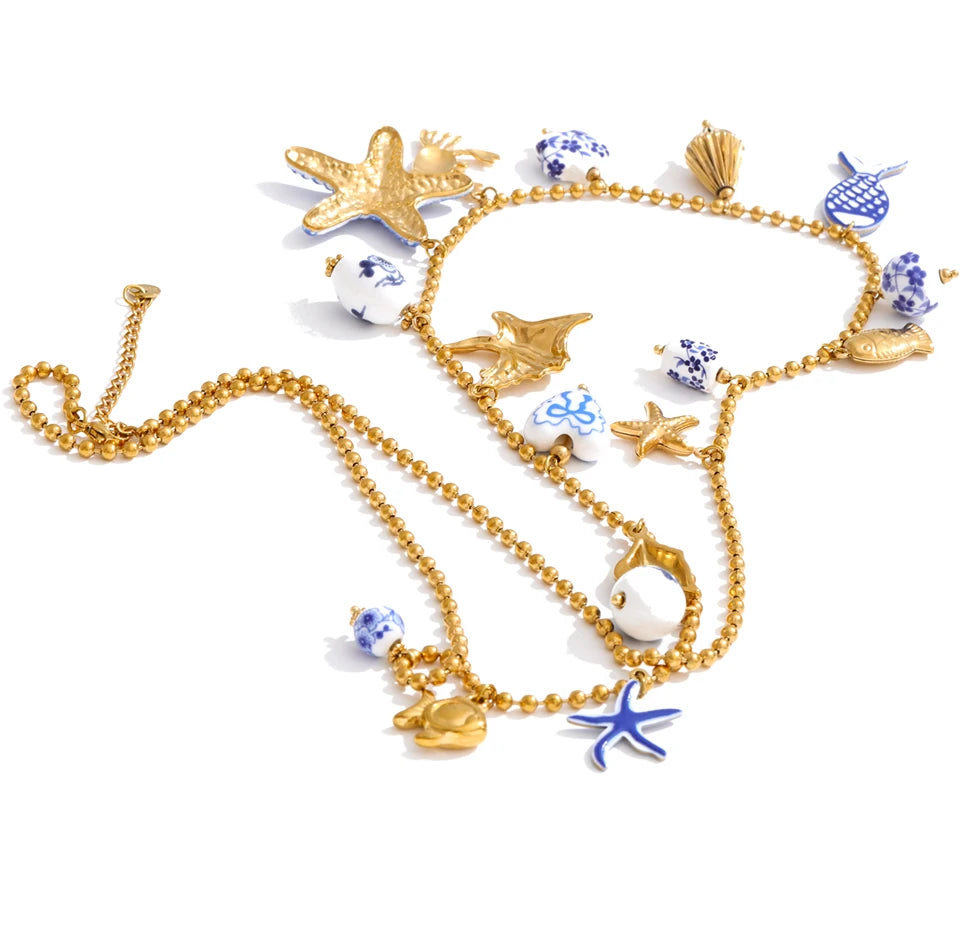 A gold beaded necklace with various sea-themed charms including starfish, seashells, a dolphin, a seahorse, and blue-and-white patterned beads, displayed on a clean white background.