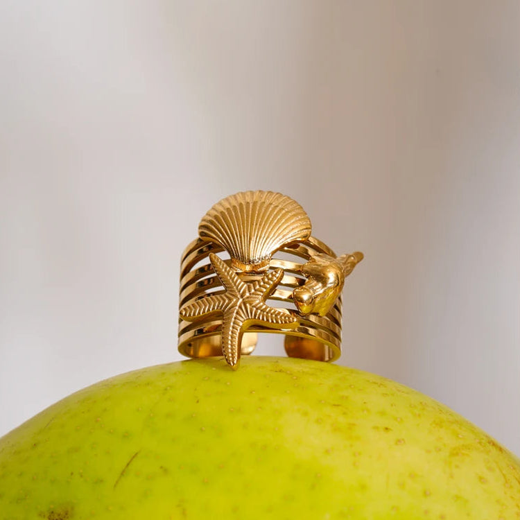 Gold ring with shell and starfish design on a green fruit