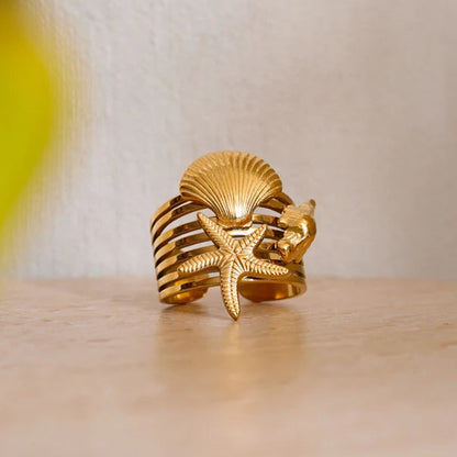 Gold ring with shell and starfish design on a wooden surface