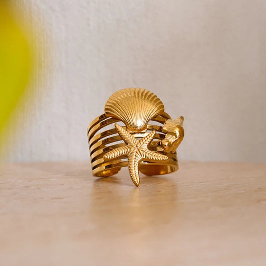 Gold ring with shell and starfish design on a wooden surface