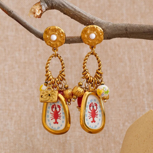 Gold earrings with lobster designs on a beige background
