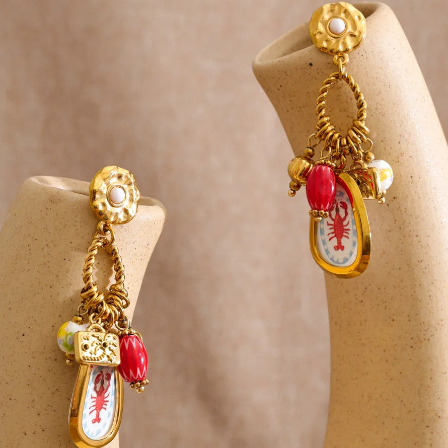 Gold earrings with red and white accents on beige earring stands against a beige background