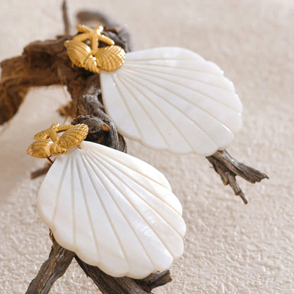 Two white shells with gold accents on a piece of driftwood against a beige background.